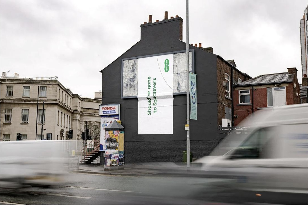 Specsavers billboard, deliberately cut off mid-frame against a New North Road shopfront